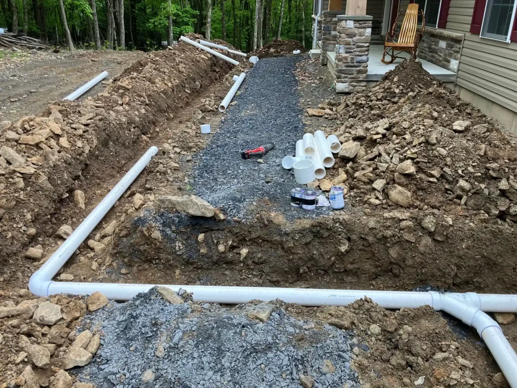 White PVC sewer pipes installed in excavated trenches beside a newly constructed home.