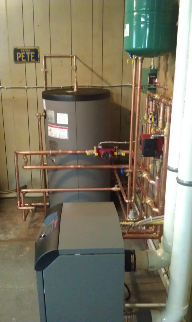 Boiler connected to a large insulated storage tank, copper piping, pumps, controls, and an expansion tank.
