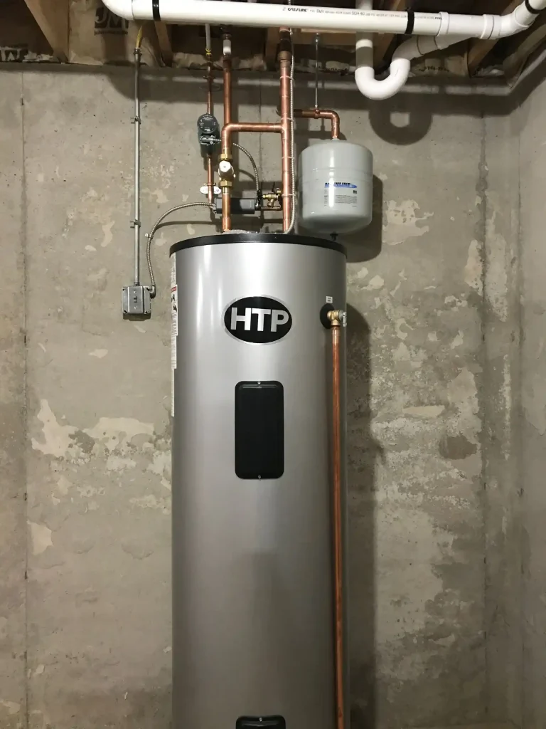 Tall HTP hot water tank connected to copper piping, a circulation pump, and a wall-mounted expansion tank.