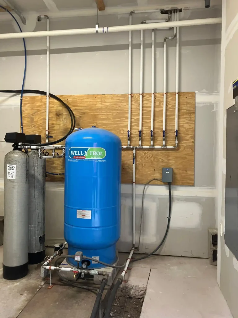 Residential well pressure tank and water filtration system with professionally installed plumbing and organized water supply piping.