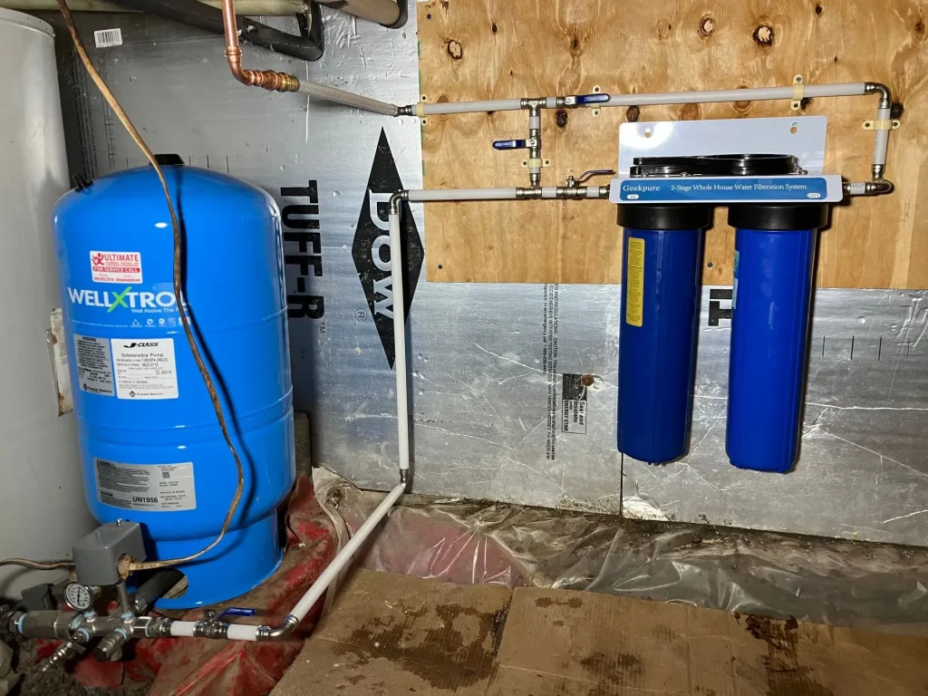 Blue well pressure tank connected to a two-stage whole-house water filtration system and supply piping.
