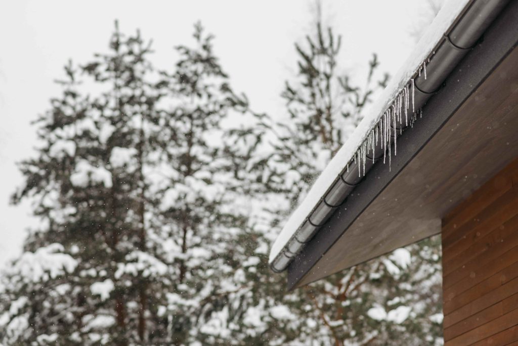 Icicles hanging from a snow-covered roof and gutter during freezing winter weather.