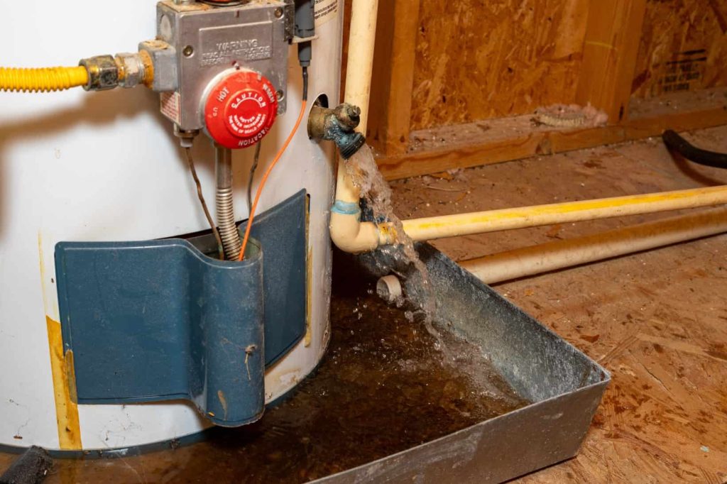 Water leaking from a corroded water heater connection into a metal drain pan.