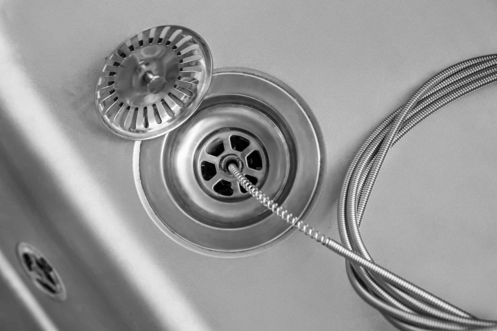 Drain snake inserted into a stainless-steel sink drain to clear a clog.