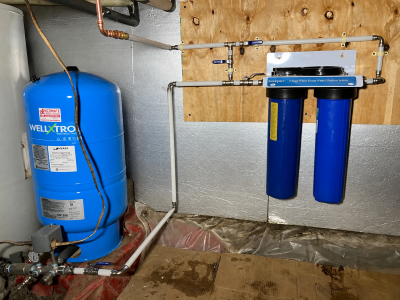Blue well pressure tank connected to a two-stage whole-house water filtration system and supply piping.